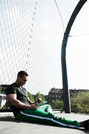 Mature man sitting on outdoor basketball court, looking at tablet computer, Germany Stock Photo - Premium Royalty-Free, Code: 600-06786842