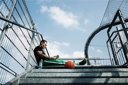 pantalon - Mature man sitting at top of stairs on outdoor basketball court looking at tablet computer, Germany Photographie de stock - Premium Libres de Droits, Code: 600-06786850