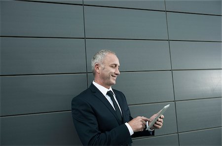 simsearch:600-06786850,k - Mature businessman standing in front of wall, looking at tablet computer Stock Photo - Premium Royalty-Free, Code: 600-06782193