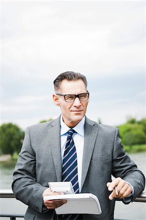 simsearch:600-06782206,k - Portrait of mature businessman standing on bridge holding documents, wearing horn-rimmed eyeglasses, Mannheim, Germany Stock Photo - Premium Royalty-Free, Code: 600-06782223