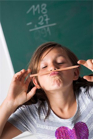 simsearch:600-07192152,k - Portrait of girl standing in front of blackboard in classroom, holding pencil over mouth, Germany Stock Photo - Premium Royalty-Free, Code: 600-06899884