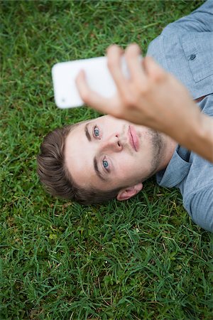 europeo (hombre) - High angle view of young man lying on grass, looking at cell phone, Germany Foto de stock - Sin royalties Premium, Código: 600-06899947