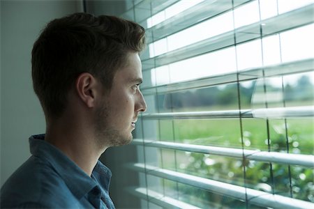 Close-up portrait of young man, looking out window through blinds, Germany Photographie de stock - Premium Libres de Droits, Code: 600-06899990