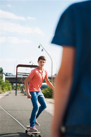 simsearch:600-07584761,k - Teenage boy skateboarding on road with back of another boy in foreground, Germany Stock Photo - Premium Royalty-Free, Code: 600-06961028