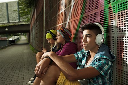 Children sitting next to wall outdoors, wearing headphones and listening to music, Germany Stock Photo - Premium Royalty-Free, Code: 600-07117180