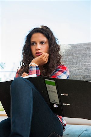 Teenage girl sitting on floor next to sofa, thinking and writing in binder, Germany Stock Photo - Premium Royalty-Free, Code: 600-07148162