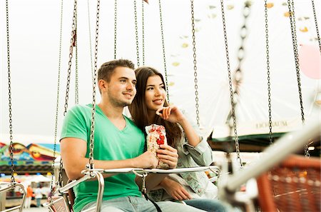 Young couple sitting on amusement park ride eating popcorn, Germany Stock Photo - Premium Royalty-Free, Code: 600-07156197