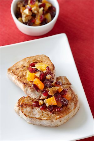 pork - Porkchops on Plate dressed with Cranberries, Walnuts, and Dried Apricots, Bowl of extra Dressing in the background Stock Photo - Premium Royalty-Free, Code: 600-07204030