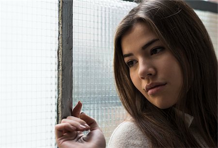 Close-up portrait of young woman standing in front of window, day dreaming and looking into the distance, Germany Photographie de stock - Premium Libres de Droits, Code: 600-07278935