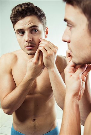 simsearch:600-06505870,k - Close-up of young man looking at reflection in bathroom mirror and examining skin on face, studio shot on white background Foto de stock - Sin royalties Premium, Código: 600-07278939