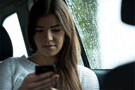 Young woman sitting inside car and looking at cell phone, on overcast day, Germany Stock Photo - Premium Royalty-Free, Code: 600-07278933