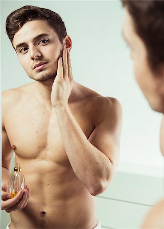 Close-up of young man looking in bathroom mirror applying cologne to face, studio shot Photographie de stock - Premium Libres de Droits, Code: 600-07278948