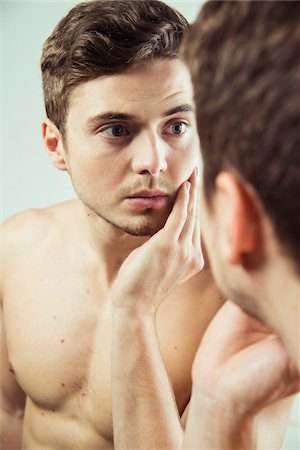 Close-up of young man looking at reflection in bathroom mirror, studio shot Photographie de stock - Premium Libres de Droits, Code: 600-07278942
