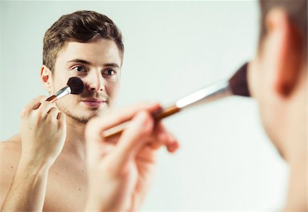 Close-up of young man looking in bathroom mirror, applying powder to face with brush, studio shot on white background Foto de stock - Sin royalties Premium, Código: 600-07278951