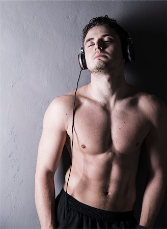 Portrait of young man wearing headphones and listening to music, studio shot on grey background Stock Photo - Premium Royalty-Free, Code: 600-07278964