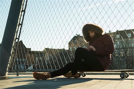 semelle (soulier) - Teenage girl sitting on skateboard outdoors, next to chain link fence near comercial dock, wearing winter coat and using smart phone, Germany Photographie de stock - Premium Libres de Droits, Code: 600-07310999