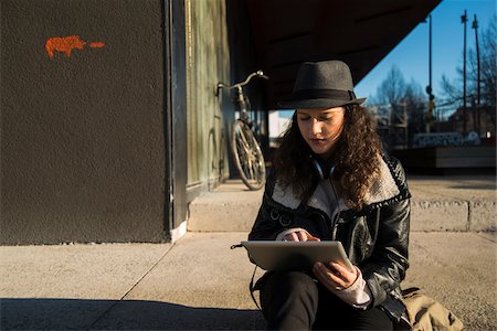 simsearch:600-07310993,k - Teenage girl sitting on curb of sidewalk outdoors, wearing fedora and using tablet computer, Germany Photographie de stock - Premium Libres de Droits, Code: 600-07310990