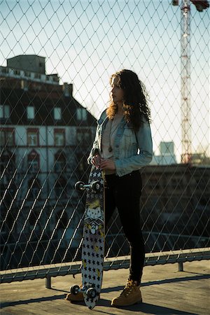 simsearch:600-07311095,k - Teenage girl standing outdoors next to chain link fence near comercial dock, holding skateboard, Germany Stock Photo - Premium Royalty-Free, Code: 600-07311000