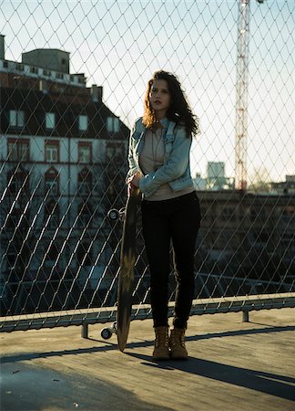 Teenage girl standing outdoors next to chain link fence near comercial dock, holding skateboard, Germany Foto de stock - Sin royalties Premium, Código: 600-07311001