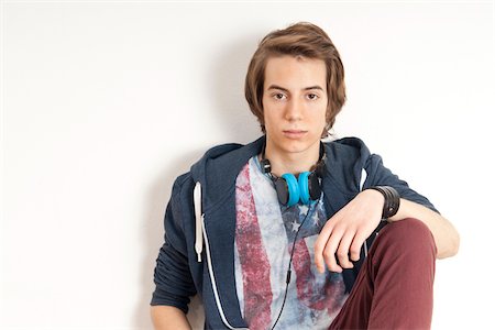 simsearch:600-06505870,k - Portrait of teenage boy sitting and leaning against wall, with headphones around neck and looking at camera, studio shot on white background Foto de stock - Sin royalties Premium, Código: 600-07311013