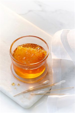 A small glass jar with clear golden honey and a honey comb with cotton swabs. High key image of honey and beauty products. Photographie de stock - Premium Libres de Droits, Code: 600-07311145