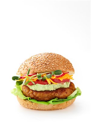 A chickpea burger on a sesame bun with lettuce, chickpeas, guacamole, shredded cheddar cheese, tomatoes, radish, and sprouts close-cut on a white background Foto de stock - Sin royalties Premium, Código: 600-07311141