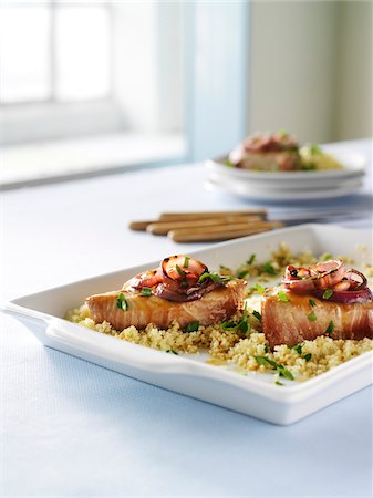 dish (shallow concave container) - Two grilled tuna steaks on cooked couscous with chopped fresh parsley and grilled red onions. Food presented on a white platter on a tabletop with steak knives in the background in a high key setting with light from window. Stock Photo - Premium Royalty-Free, Code: 600-07311150