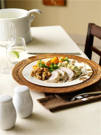 A holiday dinner plate containing turkey breast, stuffing, sweet potato, mashed potato, greens and fresh herbs. Cutlery, ice water, wine glass, salt and pepper shaker and serving dish also present on tabletop. Foto de stock - Sin royalties Premium, Código: 600-07311151