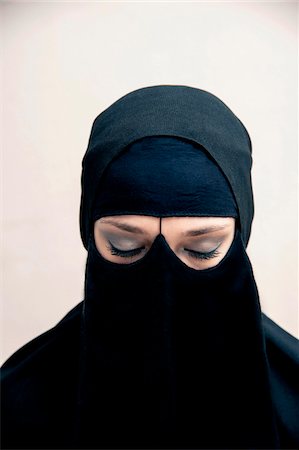 Close-up portrait of young woman wearing black, muslim hijab and muslim dress, eyes closed showing eye makeup, studio shot on white background Stock Photo - Premium Royalty-Free, Code: 600-07434924