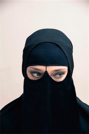 Close-up portrait of young woman wearing black, muslim hijab and muslim dress, eyes looking to the side showing eye makeup, studio shot on white background Foto de stock - Sin royalties Premium, Código: 600-07434926