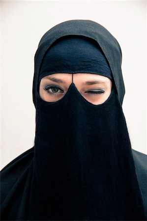 simsearch:6109-06005678,k - Close-up portrait of young woman wearing black, muslim hijab and muslim dress, winking and looking at camera, eyes showing eye makeup, studio shot on white background Photographie de stock - Premium Libres de Droits, Code: 600-07434927