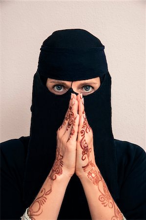 simsearch:600-07434925,k - Close-up portrait of woman wearing black muslim hijab and muslim dress looking at camera, with hands praying and showing arms and hands painted with henna in arabic style, studio shot on whtie background Foto de stock - Sin royalties Premium, Código: 600-07434938