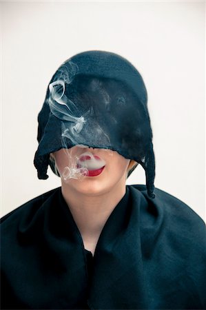 simsearch:600-07434939,k - Close-up portrait of young woman wearing black, muslim dress and black, hijab covering part of head, while blowing smoke from red lips, studio shot on white background Photographie de stock - Premium Libres de Droits, Code: 600-07434931