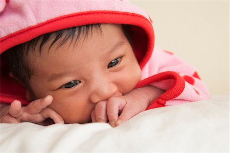 Close-up portrait of two week old Asian baby girl in pink polka dot hooded jacket, studio shot Stock Photo - Premium Royalty-Free, Code: 600-07453962
