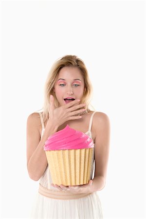 Portrait of young woman holding giant cupcake and looking surprised, studio shot on white background Stock Photo - Premium Royalty-Free, Code: 600-07487656