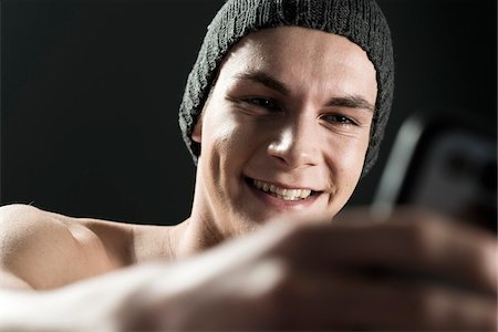 Close-up portrait of young man wearing toque, taking a selfie with cell phone, studio shot on black background Photographie de stock - Premium Libres de Droits, Code: 600-07567376