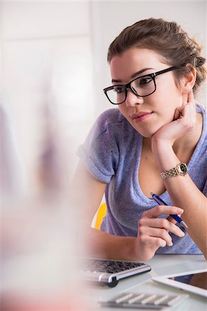 simsearch:600-06553417,k - Young woman wearing horn-rimmed eyeglasses, working in office on desktop PC, Germany Stock Photo - Premium Royalty-Free, Code: 600-07584756