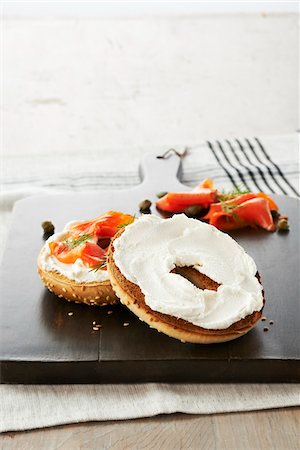 simsearch:600-00075505,k - Toasted Sesame Seed Bagel topped with Cream Cheese, Smoked Salmon, Dill and Capers on Wooden Cutting Board, Studio Shot Stock Photo - Premium Royalty-Free, Code: 600-07650789