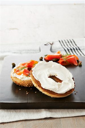 sesame bagel - Toasted Sesame Seed Bagel topped with Cream Cheese, Smoked Salmon, Dill and Capers on Wooden Cutting Board, Studio Shot Foto de stock - Sin royalties Premium, Código: 600-07650789