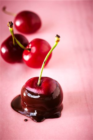Close-up of Cherry Dipped in Chocolate on Pink Background with un-dipped Cherries in the Background, Studio Shot Stock Photo - Premium Royalty-Free, Code: 600-07650795