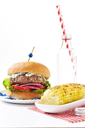 Greek style burger with spiced corn on the cob and bottle of soda with striped straws, studio shot on white background Stock Photo - Premium Royalty-Free, Code: 600-08002086