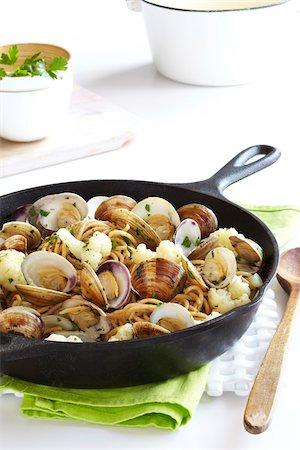 palourde - Cast iron skillet with whole wheat pasta, cauliflower and clams on a green napkin with a wooden spoon, studio shot Photographie de stock - Premium Libres de Droits, Code: 600-08002088