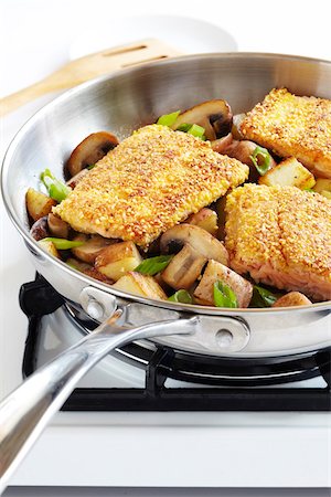 sauteeing - Cornmeal crusted trout fillets in a skillet with potatoes, mushrooms and green onions on a gas stove, studio shot Stock Photo - Premium Royalty-Free, Code: 600-08002099