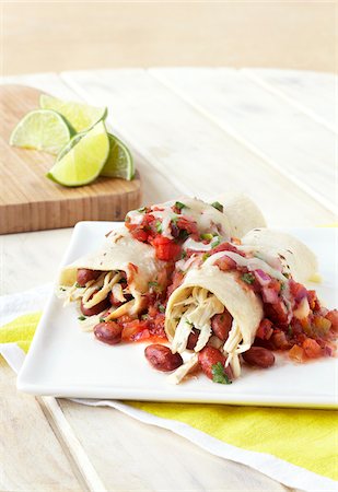 simsearch:600-08002161,k - Chicken Enchiladas with beans and salsa on a plate with limes on cutting board in the background, studio shot Stock Photo - Premium Royalty-Free, Code: 600-08002090