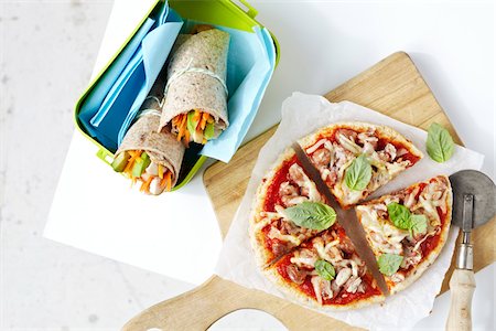 Homemade pizza on cutting board and healthy, vegetable sandwich wraps in container, studio shot on white background Stock Photo - Premium Royalty-Free, Code: 600-08002107