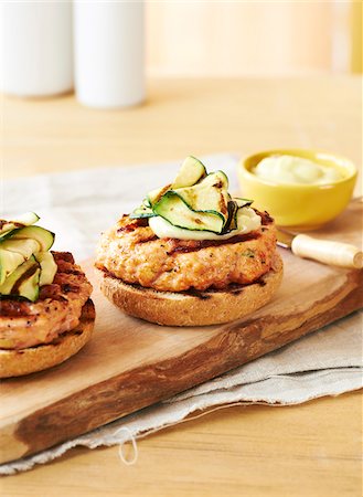 Grilled, open-faced salmon burgers with aioli and zucchini on wooden plank, studio shot Stock Photo - Premium Royalty-Free, Code: 600-08002162