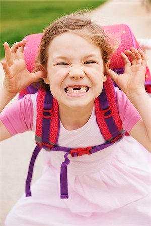 Portrait of 5 year old schoolgirl with her pink and purple school bag, making faces and looking at camera, showing her front teeth missing Photographie de stock - Premium Libres de Droits, Code: 600-08312078