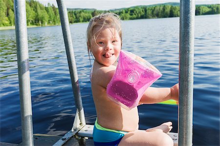 faire des grimaces - Girl with Down Syndrome wearing Water Wings Sitting on Jetty of Lake, Sweden Photographie de stock - Premium Libres de Droits, Code: 600-08519474