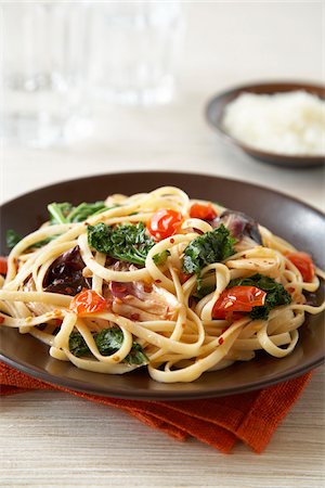 Linguine pasta with tomato, leafy greens and crushed red pepper on dark brown plate Stock Photo - Premium Royalty-Free, Code: 600-09119328