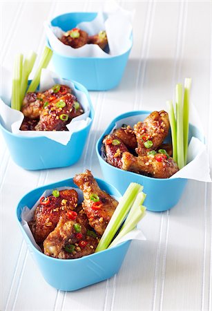 Chicken wings covered in chili and scallion sauce in blue bowls with celery sticks Stock Photo - Premium Royalty-Free, Code: 600-09119439
